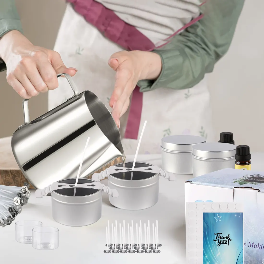 Two hands pouring melted wax from the stainless pitcher into a candle tin